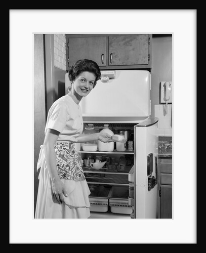 1950s Smiling Woman Housewife Putting Stick Of Butter Into Electric Refrigerator In Kitchen Looking At Camera by Anonymous