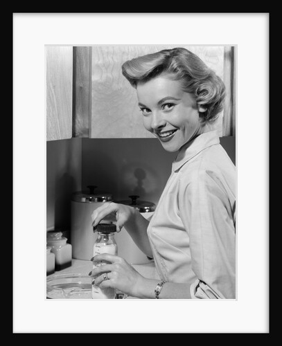 1950s Smiling Blonds Woman Mother Warming A Baby Bottle Of Milk In Kitchen Looking At Camera by Anonymous