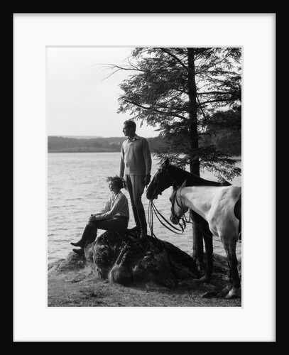 1930s Man Standing On Rock Lakeside Holding Reins Of Two Horses With Woman Seated Beside Looking Off To Side by Anonymous
