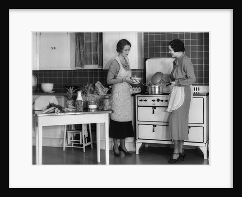 1930s Woman Housewife And Friend Wearing Apron Cooking Food In Kitchen On Gas Stove Indoor by Anonymous