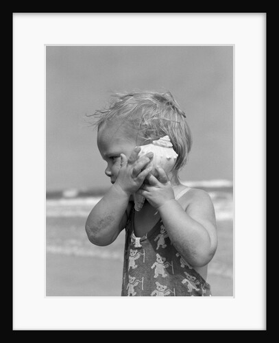 1950s Blond Toddler Girl Listening To Ocean In A Seashell Wearing Teddy Bear Bathing Suit by Anonymous