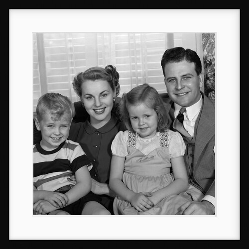 1940s 1950s Portrait Of Smiling Family Man Woman Boy Girl Sitting On Sofa Looking At Camera by Anonymous