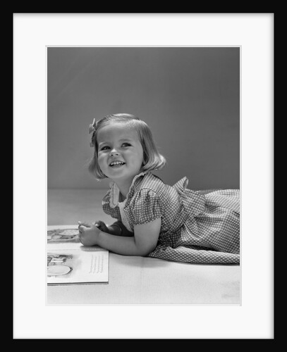 1940s Little Blond Girl Lying On Floor Looking Up And Aside Smiling From Reading A Picture Book by Anonymous