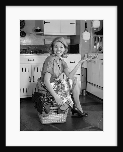 1960s smiling housewife sitting on full laundry basket by Anonymous