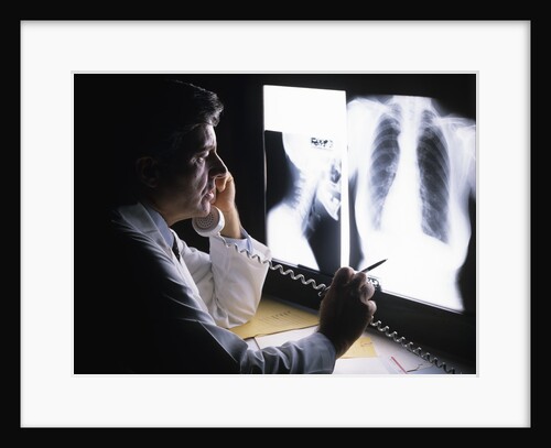 1980s doctor looking at x-ray while speaking on telephone by Anonymous