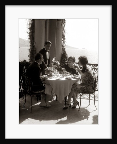 1920s group eating on balcony with waiter serving wine by Anonymous