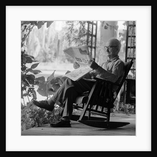 1970s elderly man reading newspaper on porch in a rocker by Anonymous