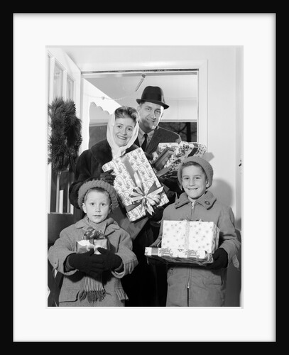 1960s family standing in doorway wearing winter coats and holding Christmas presents by Anonymous