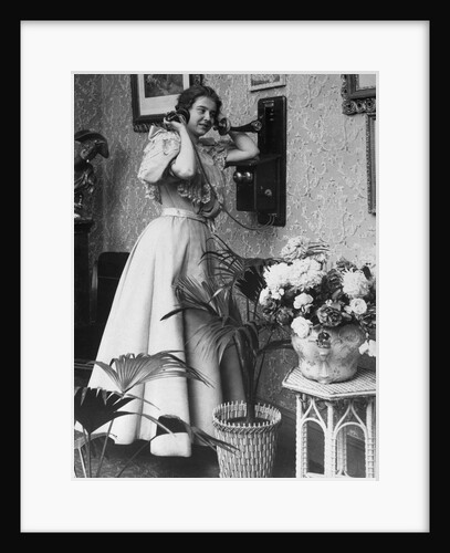 Woman Talking on Wall Mounted Telephone by Anonymous