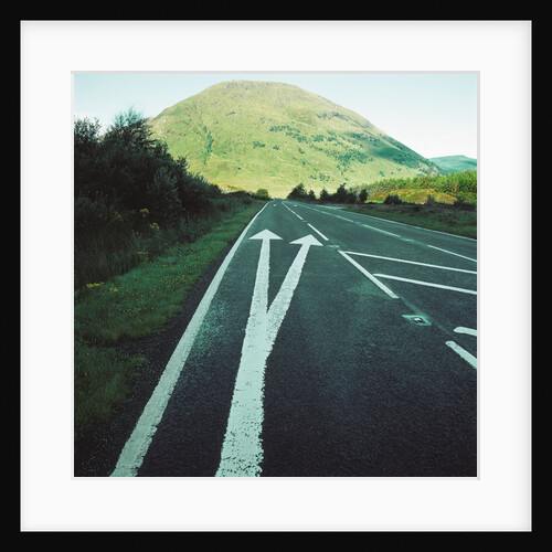 Two painted arrows on a road pointing towards a grassy mountain by Anonymous