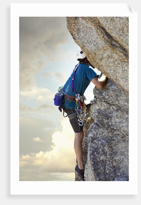 Young man rock climbing up a vertical cliff by Anonymous
