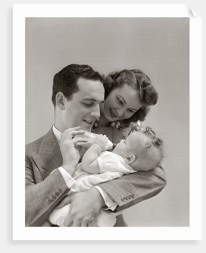 1940s Father Cradling Baby Daughter Feeding Her Bottle With Mother Looking Over His Shoulder by Anonymous