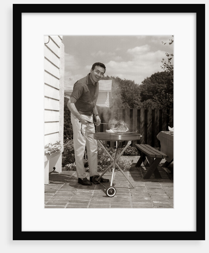 1960s Head-On View Of Man Backyard Patio Cooking Steak On Grill by Anonymous