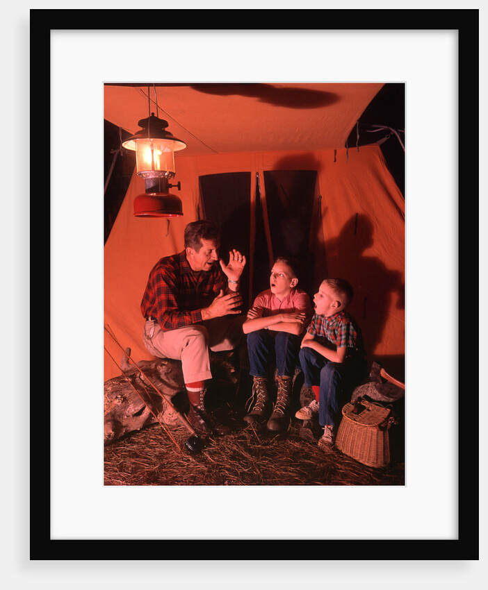 1960s 1970s Grandfather Telling Scary Story To Boys By Tent At Night Campsite In Shadows by Anonymous