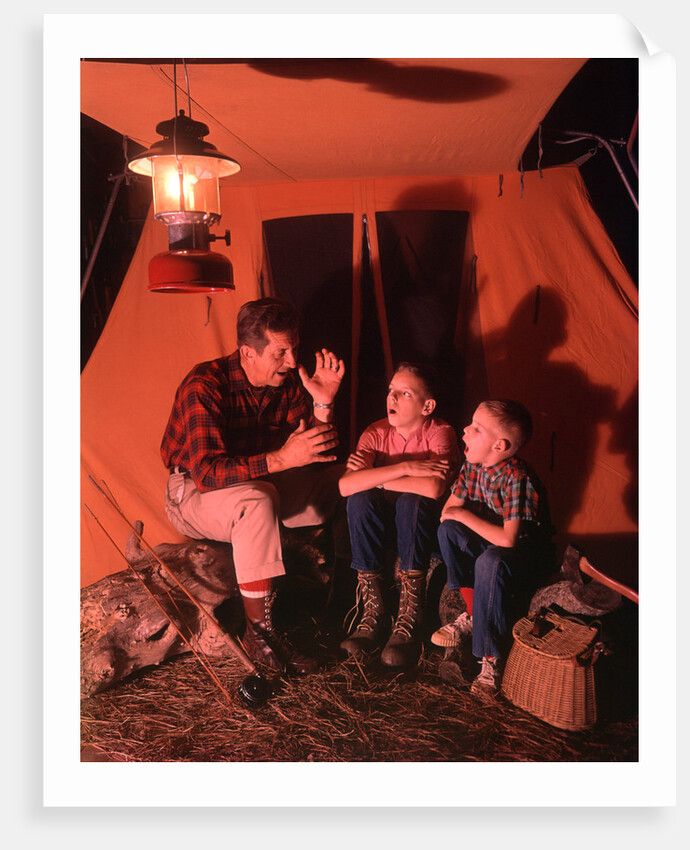 1960s 1970s Grandfather Telling Scary Story To Boys By Tent At Night Campsite In Shadows by Anonymous