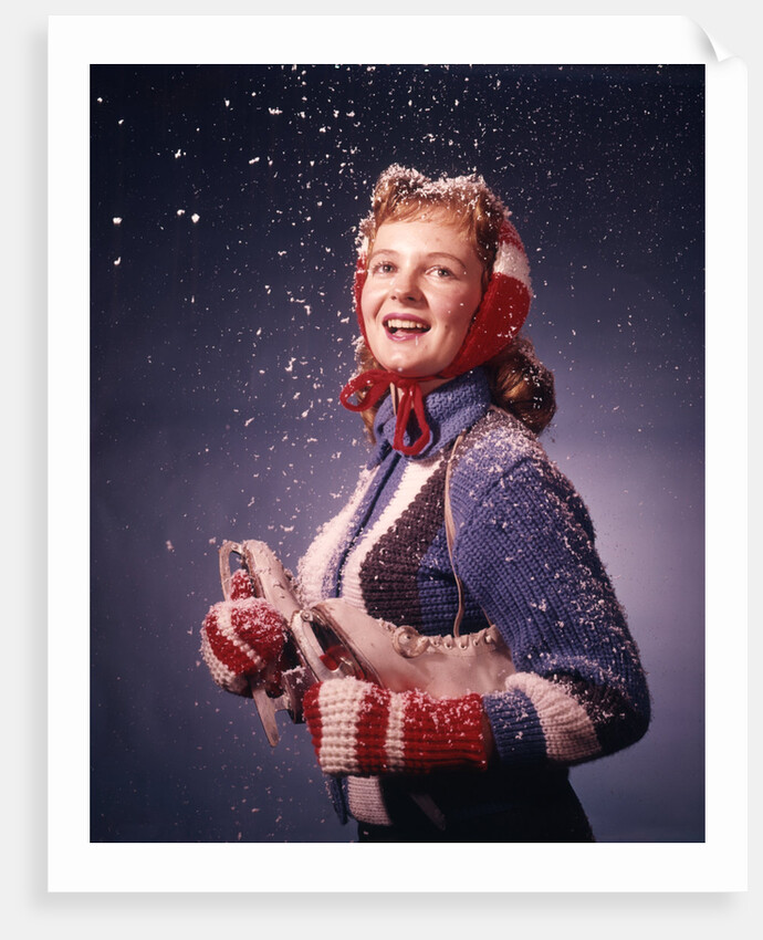 1960s Young Woman Wearing Red Mittens Ear Muffs Blue Sweater Holding Ice Skates In Falling Snow by Anonymous