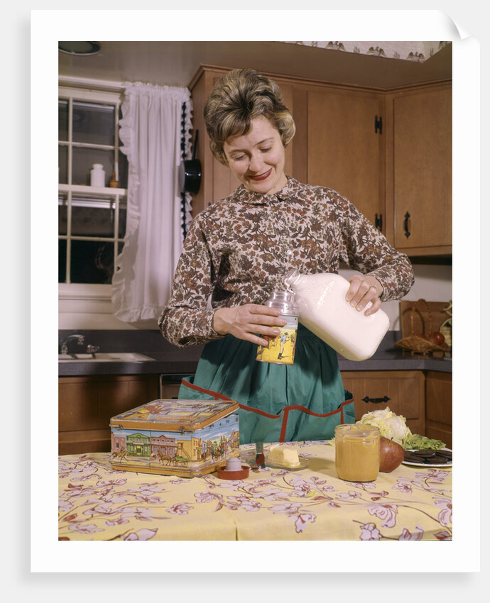 1960s Woman Housewife Mother Wearing Apron In Kitchen Pouring Milk Into Thermos For School Lunch by Anonymous