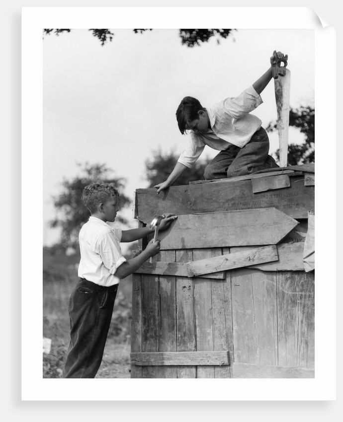 1930s Pair Of Boys Building Shack One Nailing Board To Side One On Roof With Saw by Anonymous
