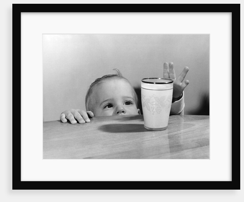 1950s Toddler Reaching Up To Table To Grab Milk Glass by Anonymous