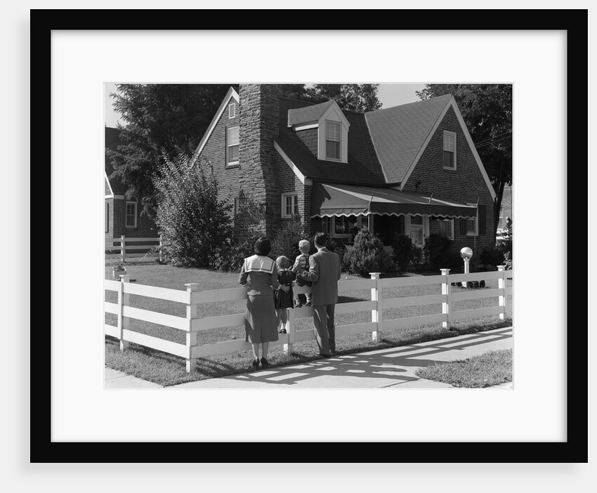 1950s Family Standing By White Fence Looking At Brick House by Anonymous