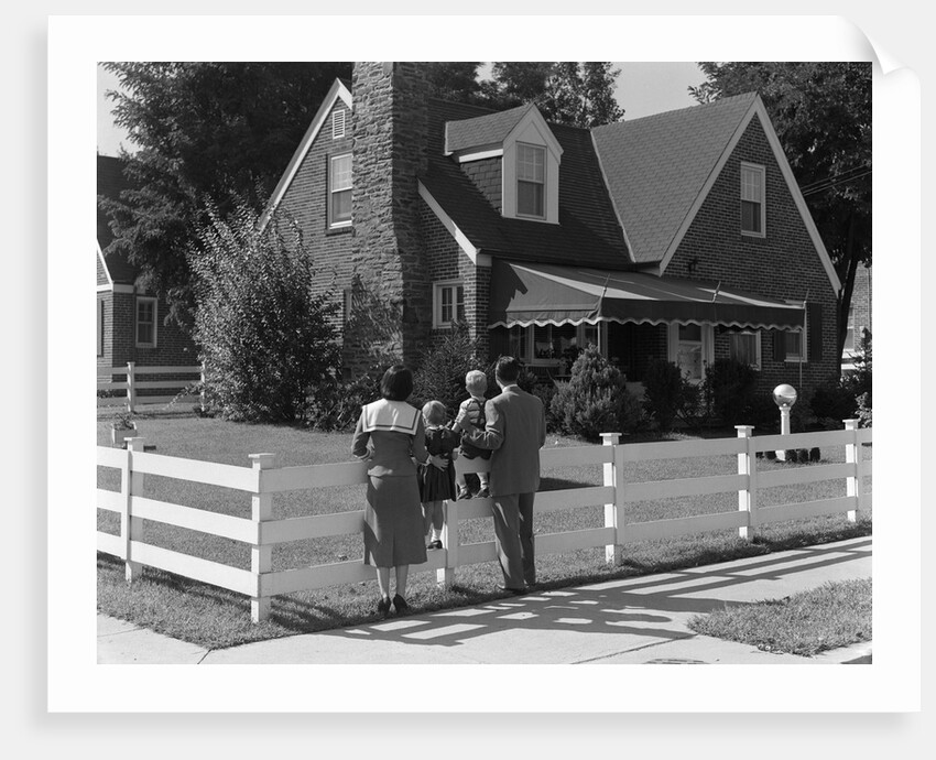 1950s Family Standing By White Fence Looking At Brick House by Anonymous