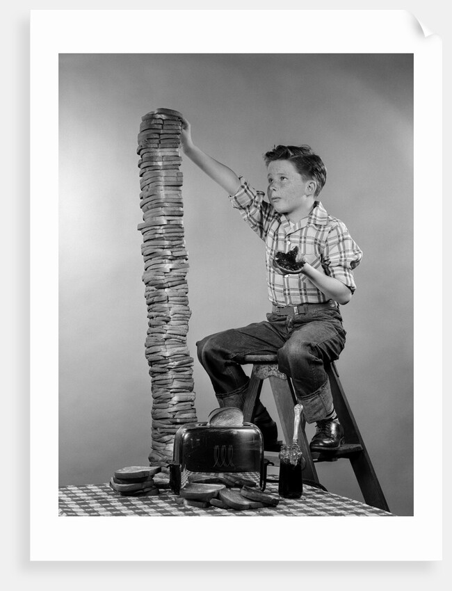 1950s Boy Eating Jelly Toast Sitting On Ladder Stacking Up Tall Pile Of Toast From Toaster by Corbis