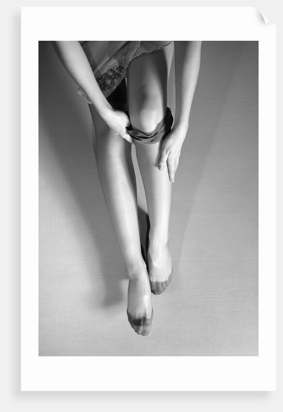 Woman's Hands Putting A Pair Of Sheer Stockings On Her Legs by Anonymous