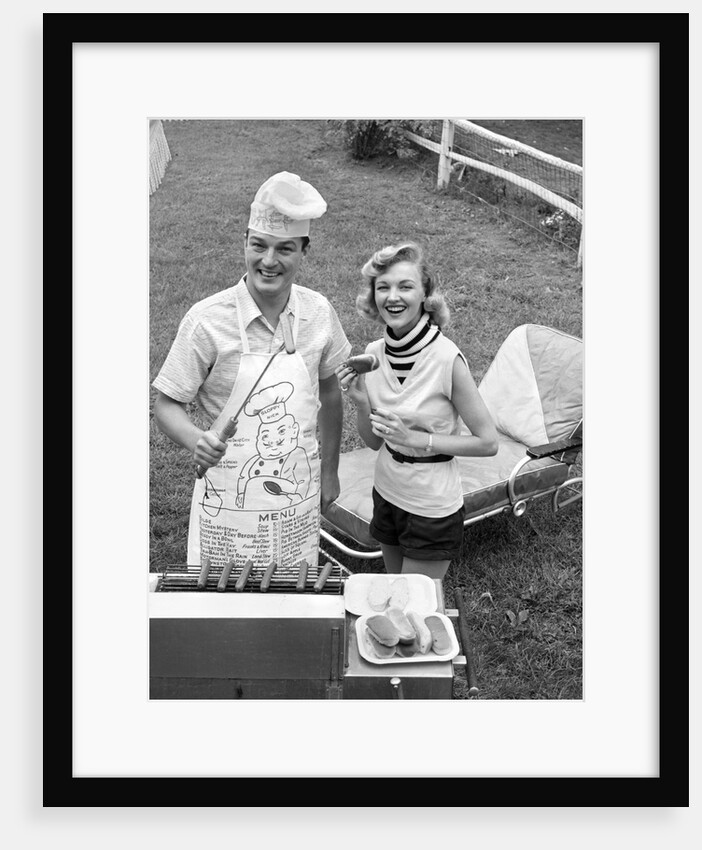 1950s Couple Backyard Grill Cook Hot Dogs Man Wearing Apron Toque and Skewered Hot Dog by Anonymous