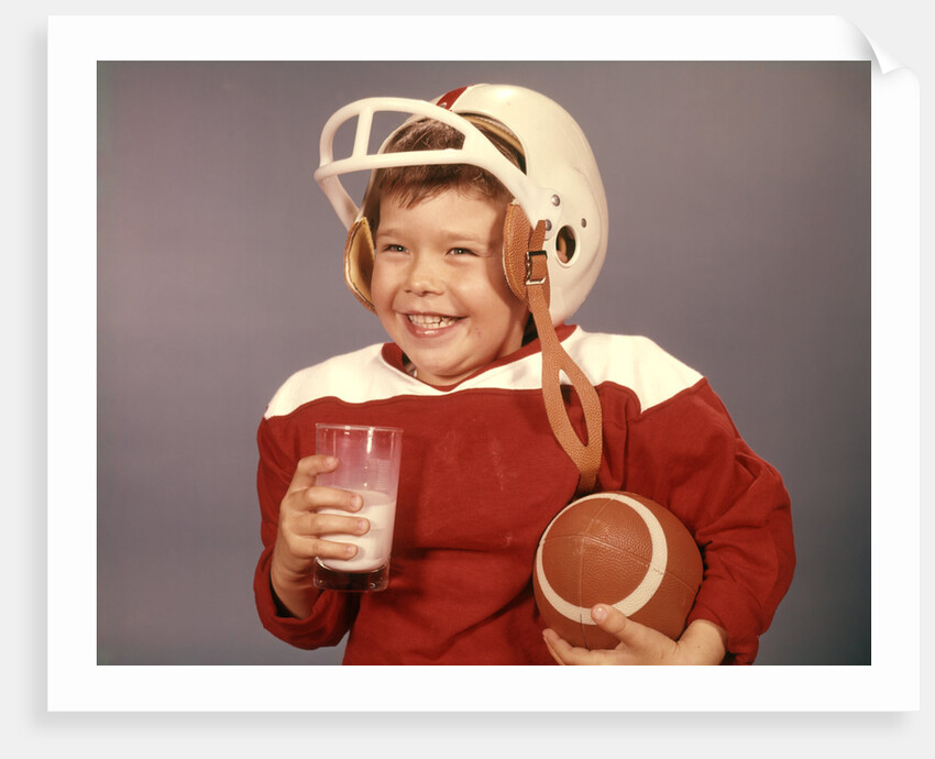 1950s 1960s Boy Drinking Milk Wearing Football Helmet Red Jersey Holding Ball by Anonymous