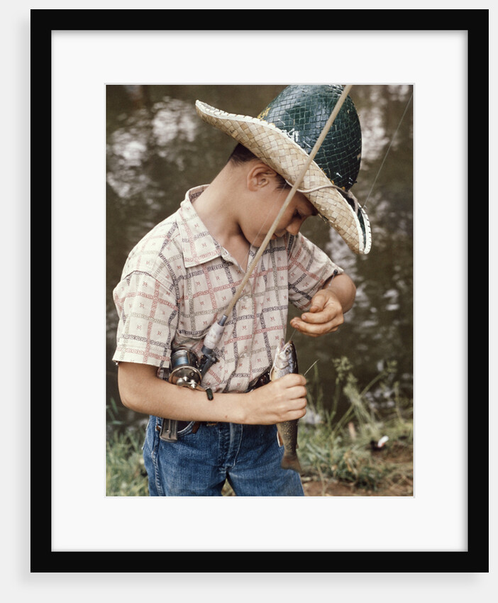 Boy Wearing Straw Hat Removing Hook From Mouth Of Fish Outdoor by Anonymous