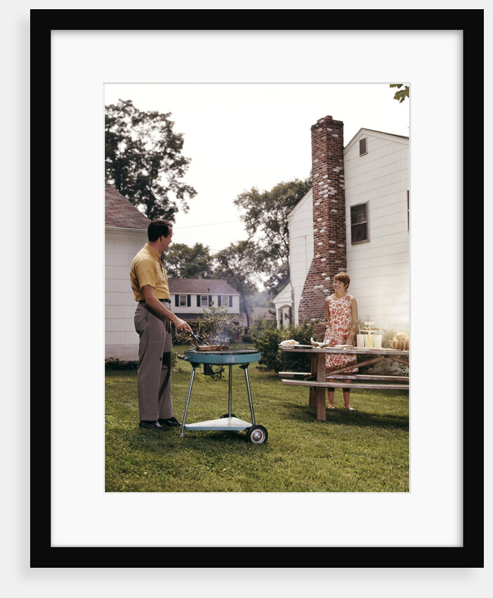 1960s Couple Suburban Backyard Man Grilling Woman Setting Picnic Table by Anonymous