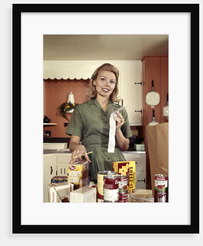 1960s Young Housewife While Checking Grocery Shopping Receipt In Kitchen by Anonymous