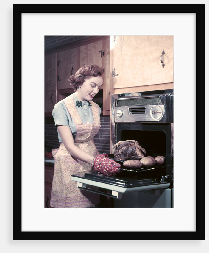 1950s Housewife Wearing Apron And Oven Mitts Taking Roast Beef With Potatoes Out Of Kitchen Oven by Anonymous