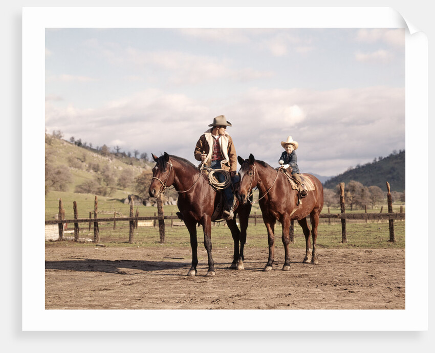 1970s Father And Son Sitting Together On Horses By Corral Wearing Hats by Anonymous