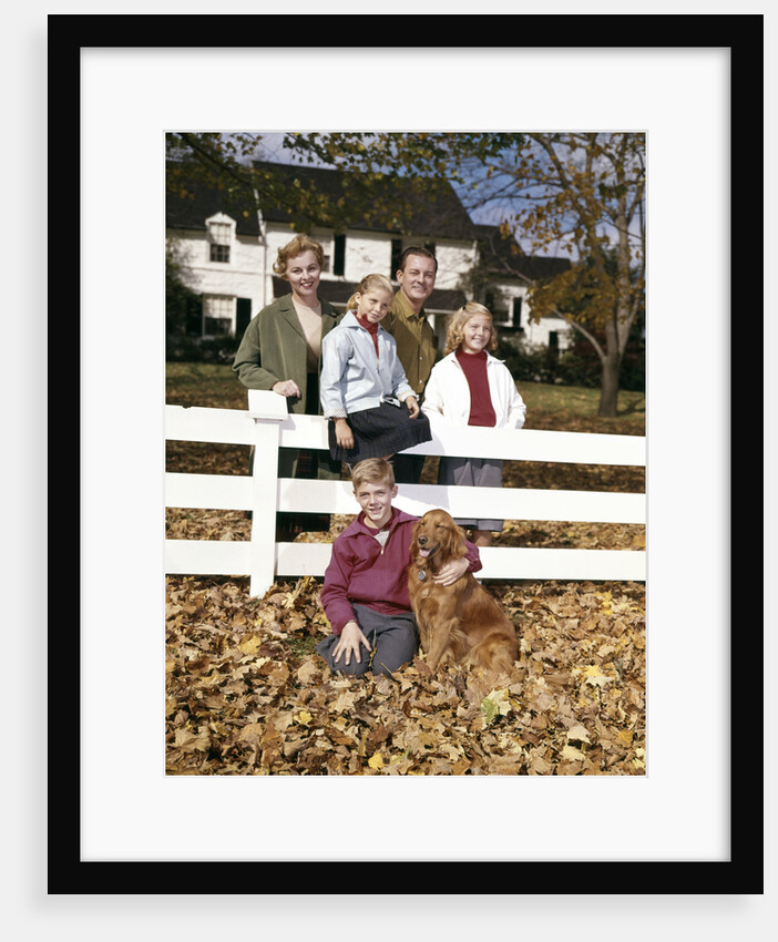 1960s Family with Dog At White Board Fence In Front Of Colonial Style Suburban House by Anonymous