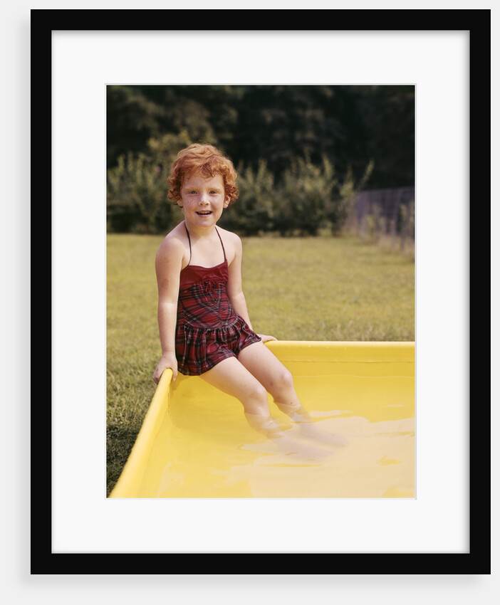 1960s Red Haired Little Girl In Plaid Bathing Suit Sitting On Yellow Plastic Backyard Swimming Pool by Anonymous