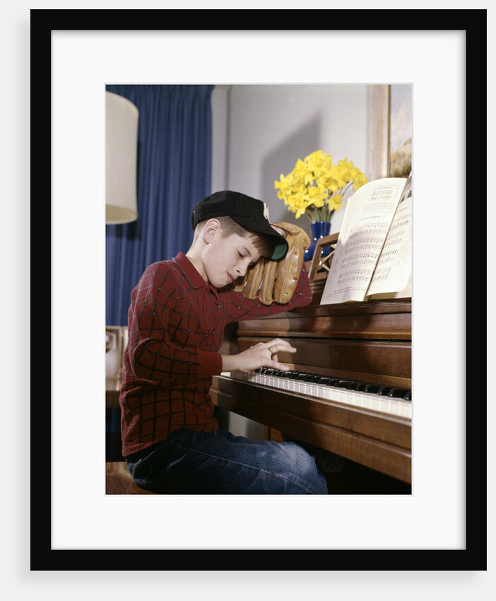 1960s 1970s Impatient Annoyed Looking Boy With Baseball Cap And Glove Practicing Piano Lesson by Anonymous
