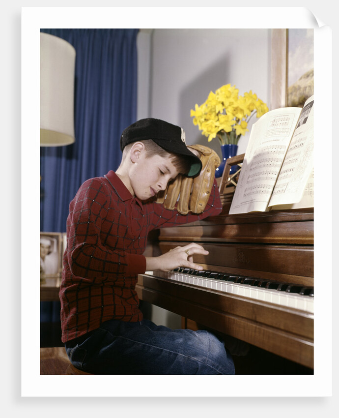 1960s 1970s Impatient Annoyed Looking Boy With Baseball Cap And Glove Practicing Piano Lesson by Anonymous