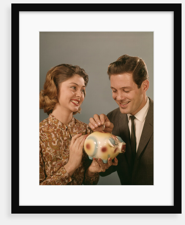 1950s 1960s Happy Couple Man Woman Putting Coins Into Savings Piggy Bank by Anonymous