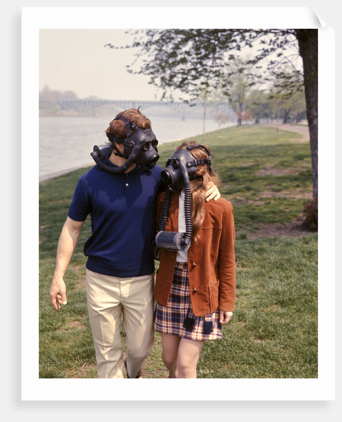 1970s Young Romantic Teenage Couple Man Woman Wearing Gas Masks Walking By River by Anonymous