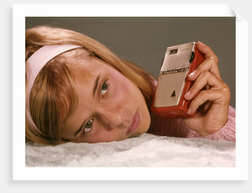 1950s 1960s Teenage Girl Holding Red Silver Small Transistor Radio To Her Ear Listening by Anonymous