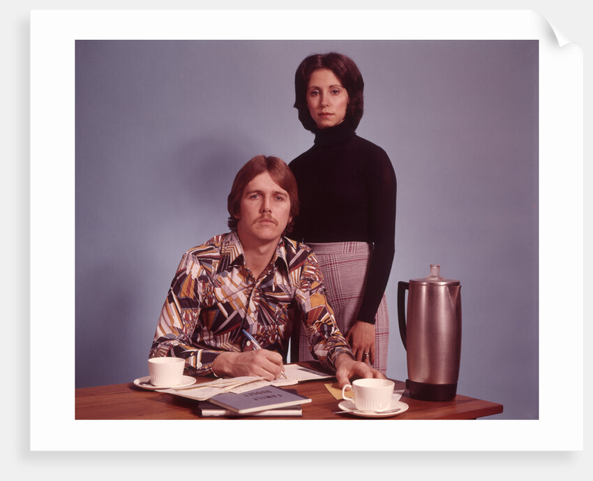 1970s Husband Wearing Loud Print Shirt Writing Family Budget and Wife Standing Behind Coffee Pot by Anonymous