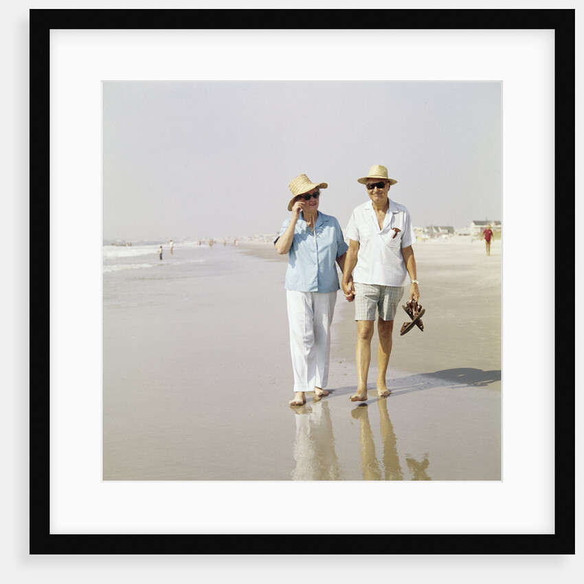 1970s Senior Couple Walking Beach Holding Hands Wearing Straw Hats by Anonymous