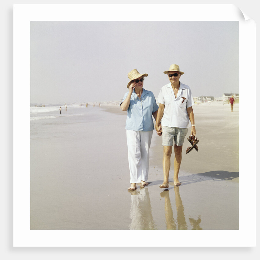 1970s Senior Couple Walking Beach Holding Hands Wearing Straw Hats by Anonymous
