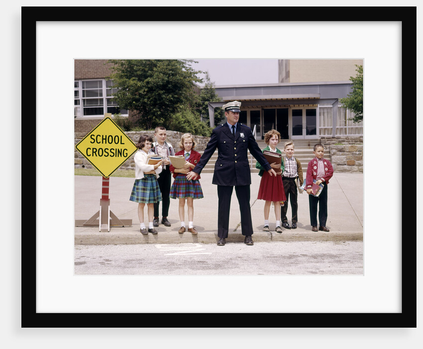 1960s Police Officer Holding Back Elementary School Children Waiting At Curb To Cross Street by Anonymous