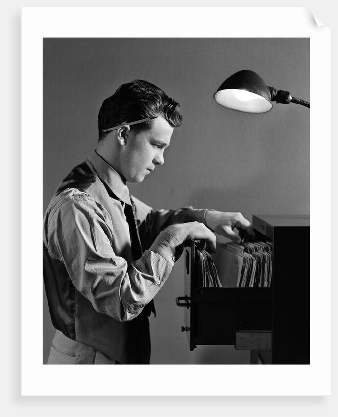 1940s Young Man Office File Clerk Putting Records Into Filing Cabinet Drawer by Anonymous
