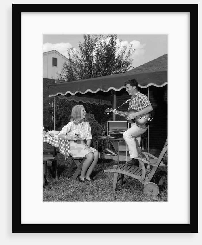 1960s Boy Playing Guitar, Woman Holding Soft Drink Bottle Outside In Backyard by Anonymous