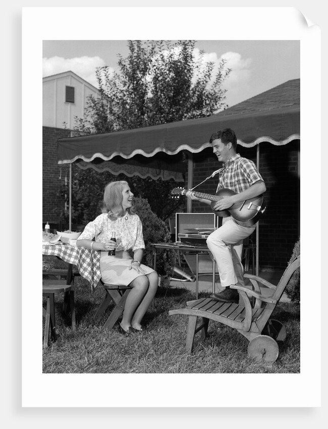1960s Boy Playing Guitar, Woman Holding Soft Drink Bottle Outside In Backyard by Anonymous