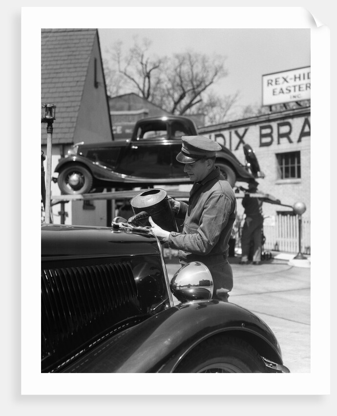 1930s Service Station Attendant In Cap and Coveralls Pouring Water From Spouted Can Into Automobile Radiator by Anonymous