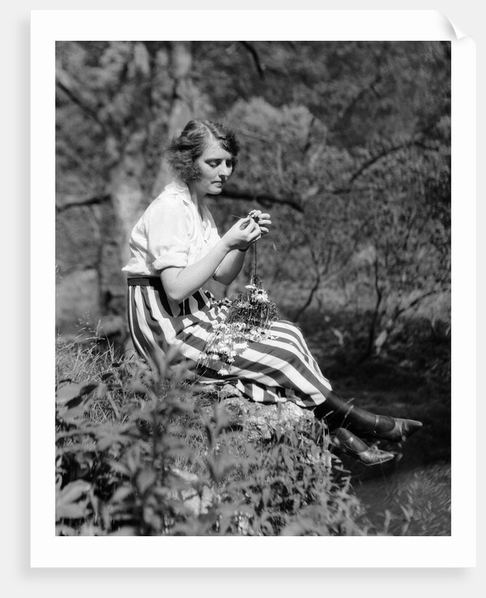 1920s Young Woman In Striped Skirt Sitting On Stream Bank In Woods Braiding Garland Of Wild Flowers by Anonymous